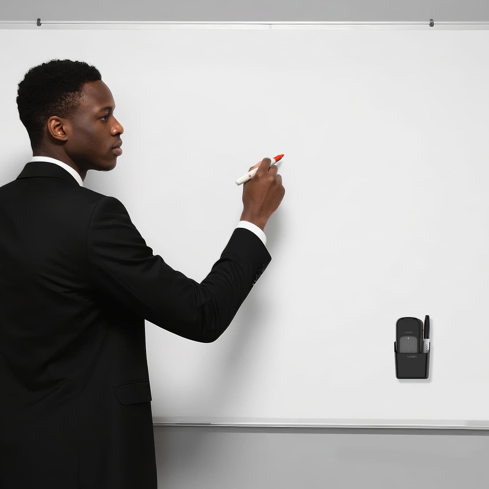 A businessman in a black suit is writing on a large, clean white magnetic whiteboard with a red marker. The black loukin All-in-One Eraser (W3543K) is magnetically attached to the bottom right of the board, securely holding a dry-erase marker and showing convenient, hands-free storage for accessories.