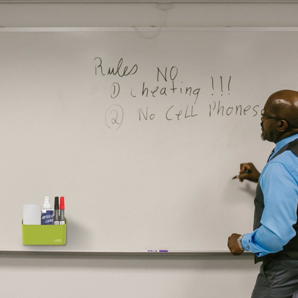 loukin W4102 MarkerHolderSmall in lime green, magnetically attached to a large white whiteboard in a classroom or office setting. The holder is shown storing an eraser, cleaner spray bottle, and markers (red and black) while a man in a blue shirt writes a list of rules on the whiteboard, demonstrating its use as a convenient magnetic accessory tray.