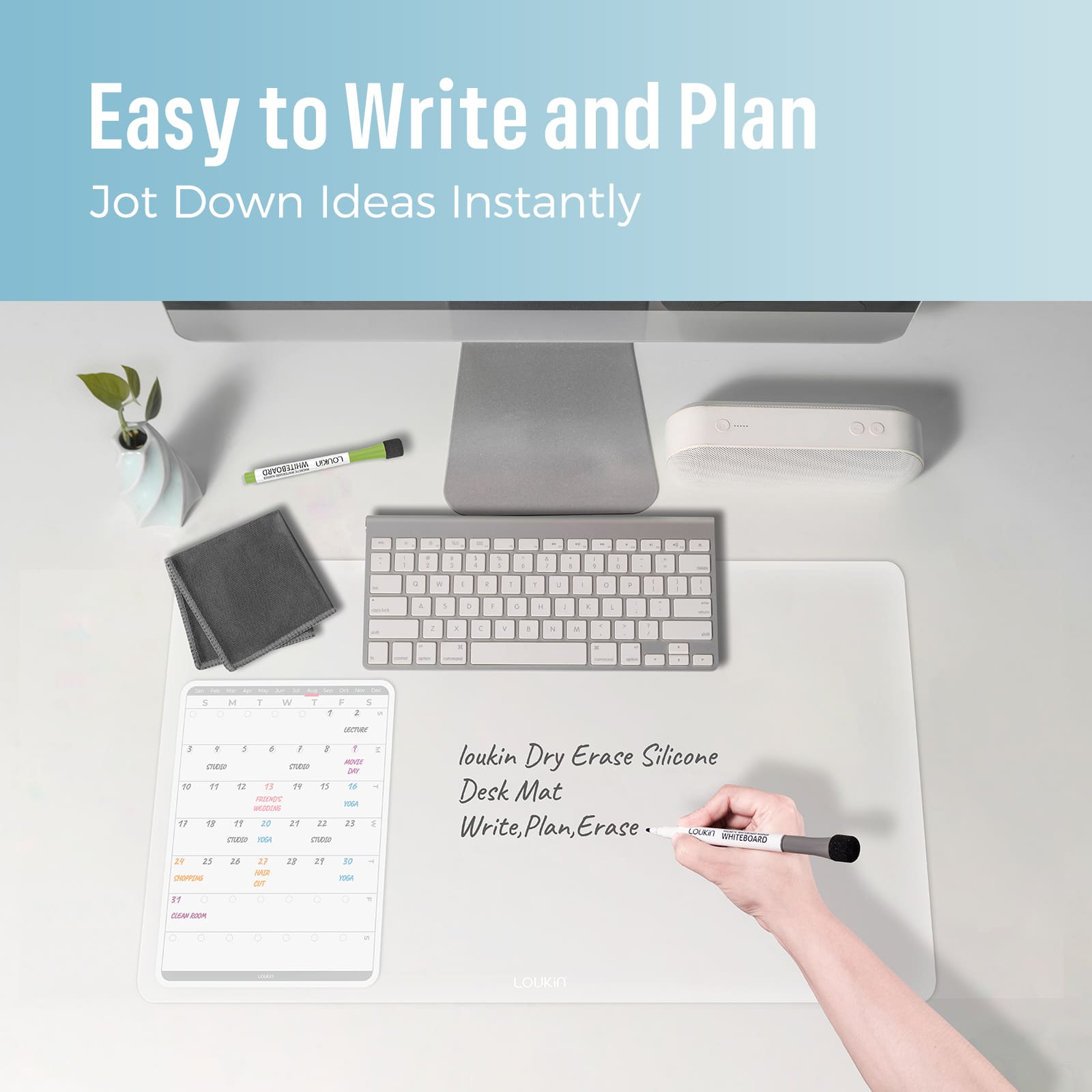loukin W1402K Dry Erase Silicone Desk Mat in use on a wooden desk beneath a monitor, highlighting the "Easy to Write and Plan" and "Jot Down Ideas Instantly" features. A hand is shown writing notes directly onto the mat next to the built-in calendar/planner template. Cleaning accessories and colored markers are visible nearby.
